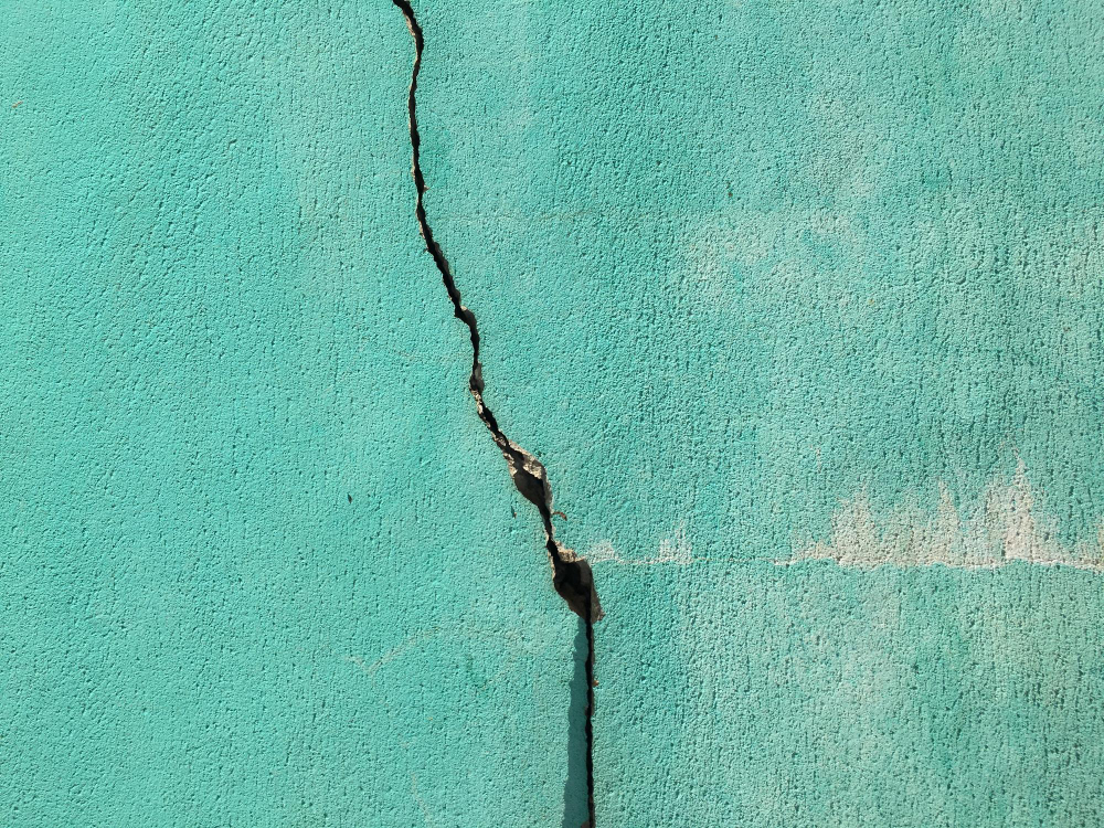 A vertical crack in a turquoise wall, illustrating how a crisis exposes the pre-existing structural weaknesses in an organisation’s communication system.
