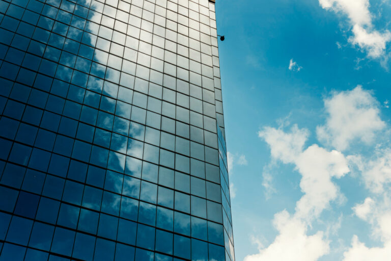 Fachada de rascacielos corporativo de cristal reflejando el cielo, simbolizando la opacidad digital de las grandes empresas del IBEX-35