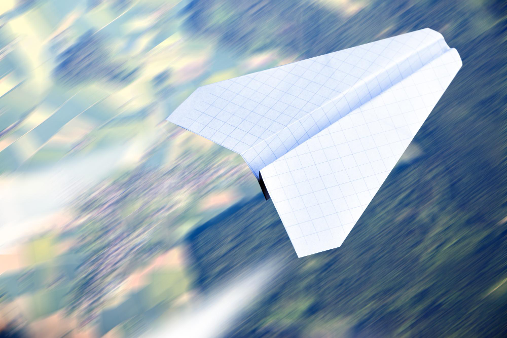 Avión de papel de cuaderno volando con dirección clara sobre un paisaje, en movimiento