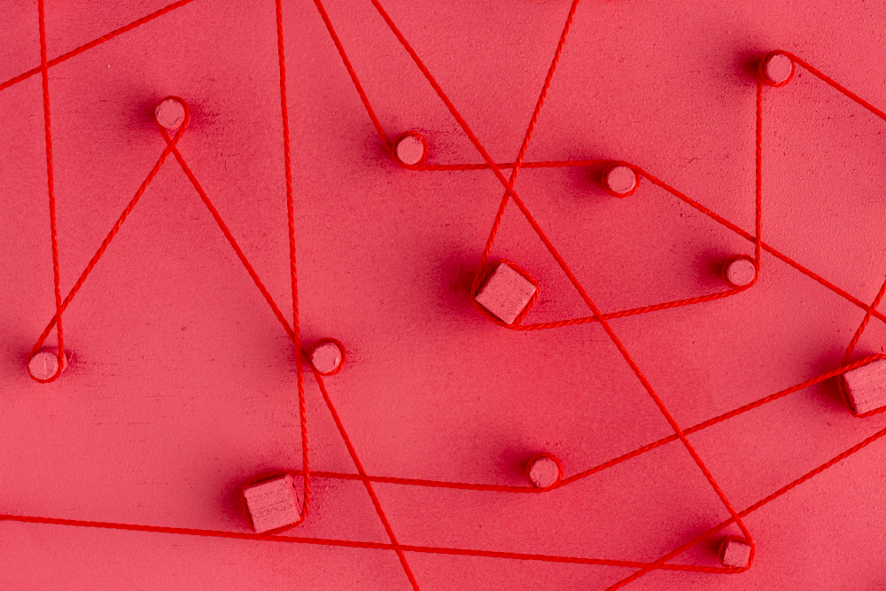Hilos rojos conectando puntos sobre superficie roja, representando relaciones entre datos e información